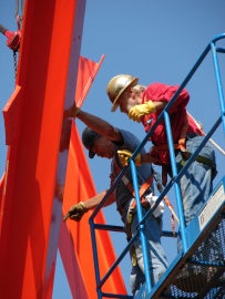 Men working on a large red metal sculpture