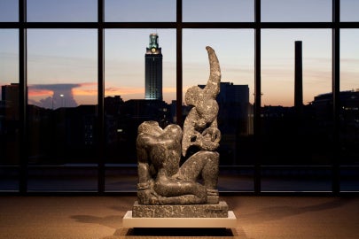 A stone sculpture in front of a window with a clock tower outside