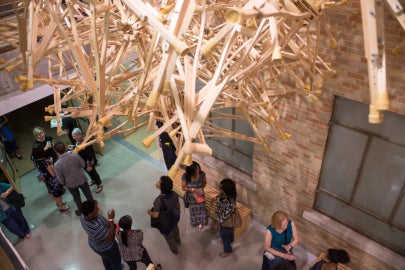 People socializing underneath a hanging sculpture made of wooden crutches
