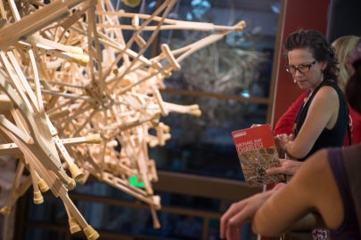 People looking at a hanging sculpture made out of wooden crutches