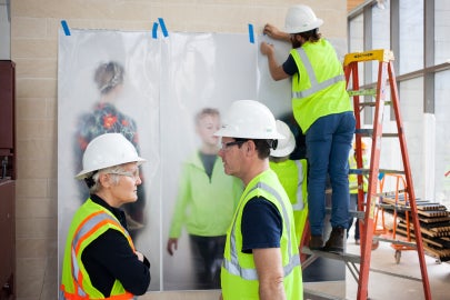 people standing in front of photos on wall and person on latter