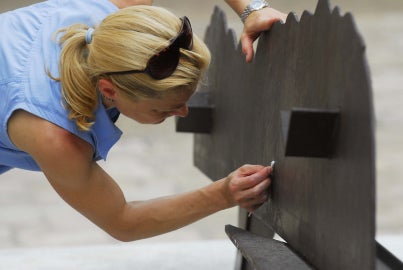 Woman in blue shirt leaning down to q-tip a brown flat sculpture