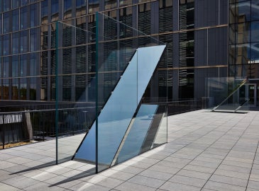 An image of Sarah Oppenheimer's "C-010106" which includes two glass planes which reflect the sky.