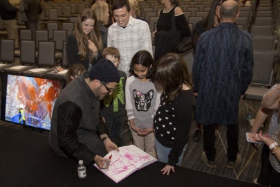 person looking down at paper while surrounded by kids and adults