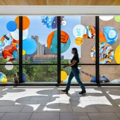 Interior view of "Autobiography: Circles" with a person walking past a brightly lit window with colored circles on the facade