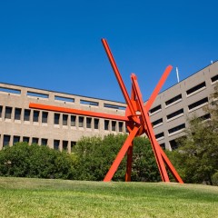A large sculpture in front of a grey building and blue sky