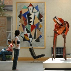 A person standing looking at a red horse sculpture indoors