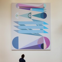 An image of Eamon Ore-Giron's "Tras los ojos," a large digital print which hangs in the atrium of a building. A man sits on a bench in front of the work.