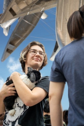 A photograph of a student holding a rabbit under Nancy Rubins' "Monochrome for Austin"