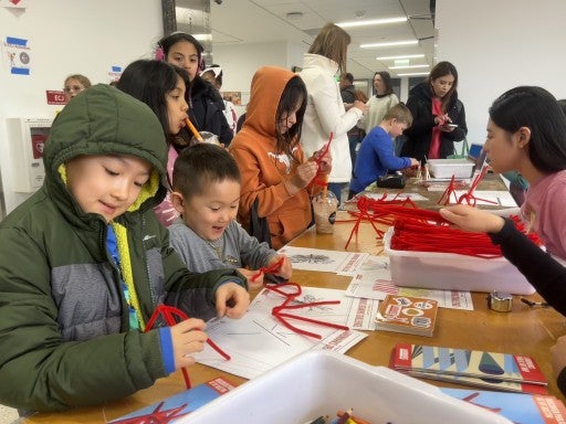 Young students stand at a table making sculptures out of pipe cleaners.