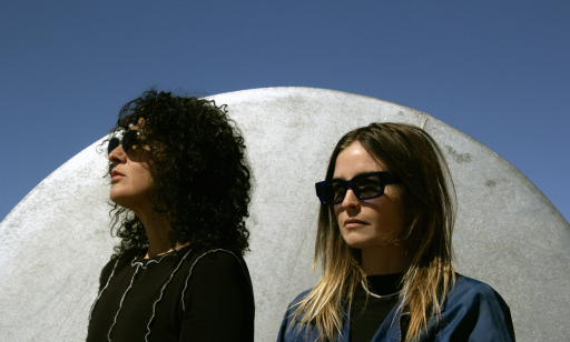 Two women wearing sunglasses pose in front of a concrete dome.