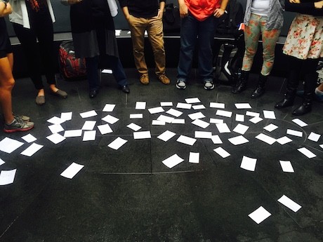 Papers scattered on the floor with students standing around them