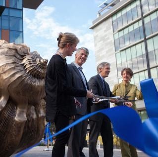 Four people cutting a ribbon in front of large bronze shell sculpture