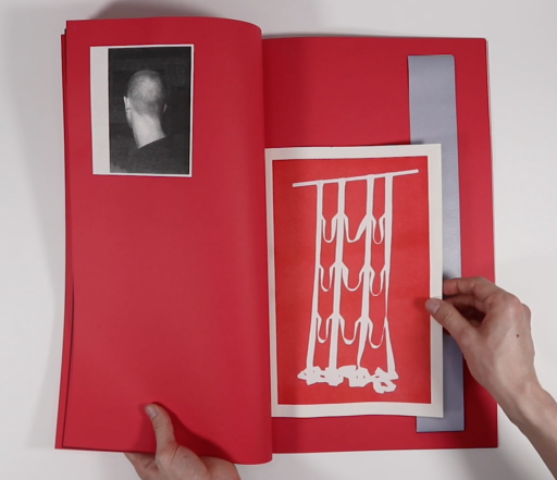 An open book which is predominantly red. On the left page there is a black and white print of the back of a head and on the right the are a red print depicting a broken grid and a strip of fabric. 