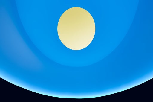 An image of the interior of James Turrell's skyspace with blue color lighting the walls, turning the visible sky yellow through the oculus. 