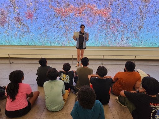 A photo of a person talking to children sitting on the floor in front of Jennifer Steinkamp's "EON"