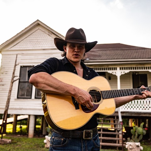 A photograph of musician Coleman Jennings holding a guitar.