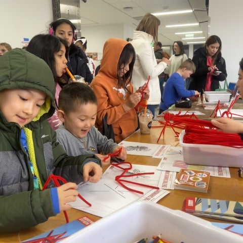 Young students stand at a table making sculptures out of pipe cleaners.