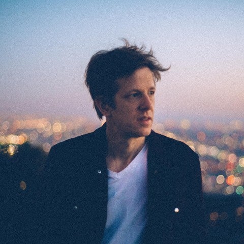 A headshot of Britt Daniel in front of a hazy sunset. 