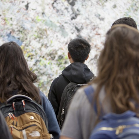 photo of students looking at a work of art that contains grey, blue, and green streaks of color across a wall