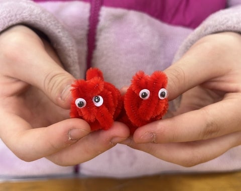A young visitor holding two small pipe cleaner sculptures with googly eyes.
