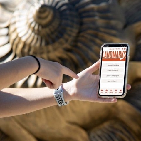 A hand points at an iphone with Landmarks' app interface showing. 