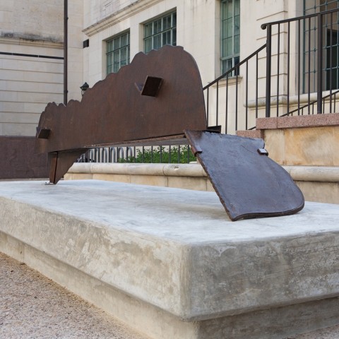 A horizontal steel sculpture which "stands" on two "legs" which are located at each end of the sculpture. The upper ridge of the sculpture begins to resemble a landscape.