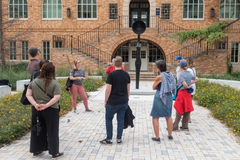 A group of people surround a sculpture by Simone Leigh. The sculpture, "Sentinel IV" is an elongated female form with a "bowl crown" in place of a head.