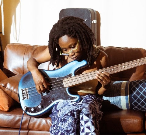 Vonne sits and plays a guitar on a couch.