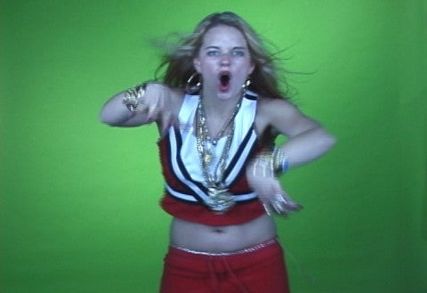 A woman dancing in front of a green wall.