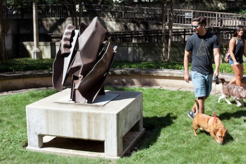 people walking dogs in front of sculpture