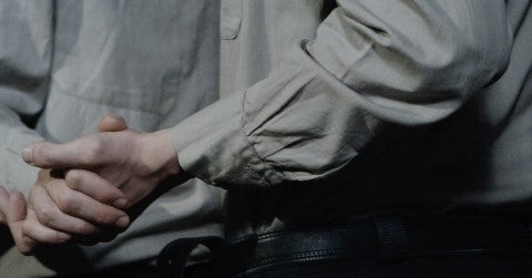 A still from Polina Kanis' "Celebration" which shows two figures shaking hands with both figures wearing grey clothing