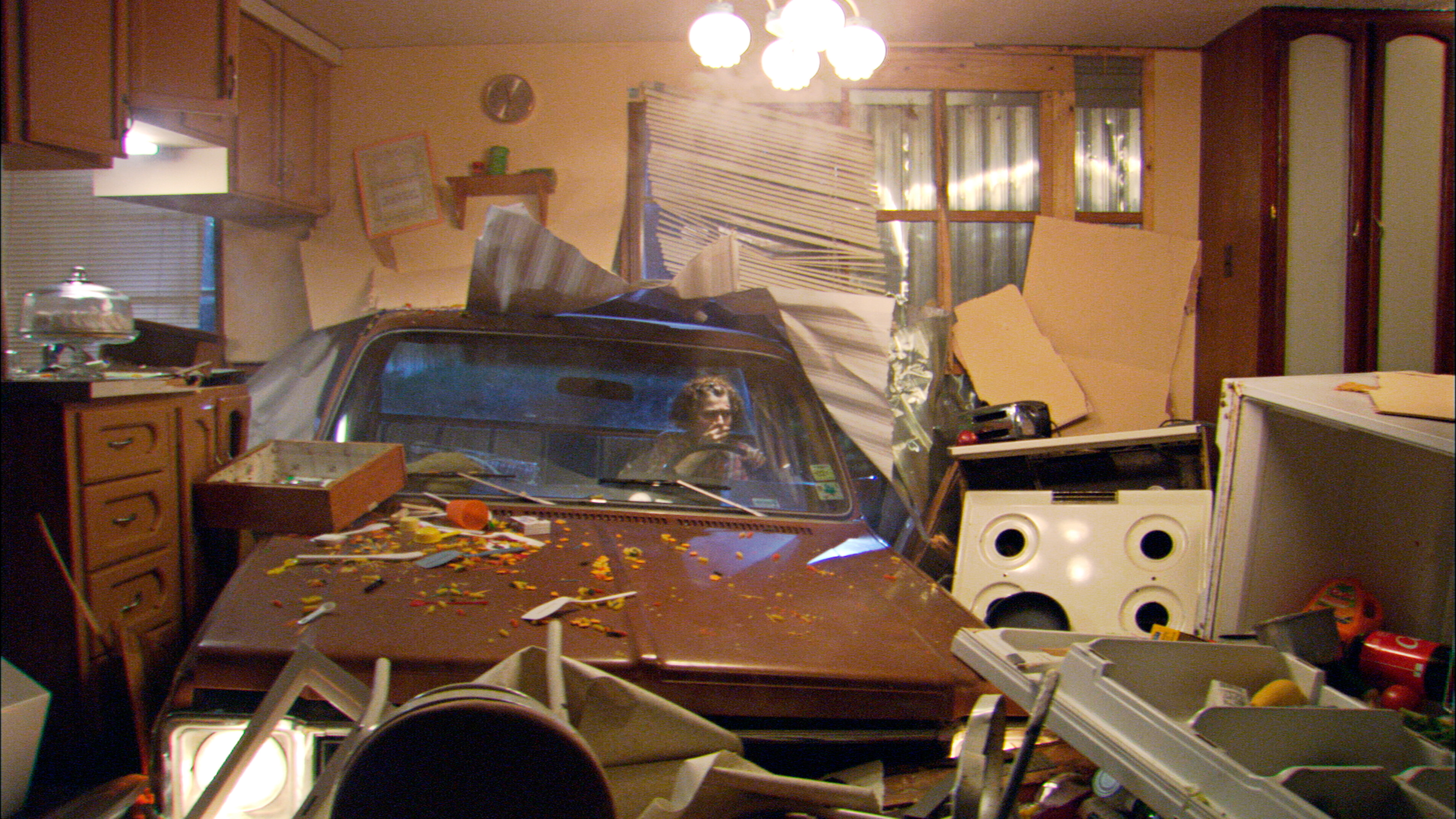 A still of "Single Wide" in which a car has crashed through a single wide trailer. 