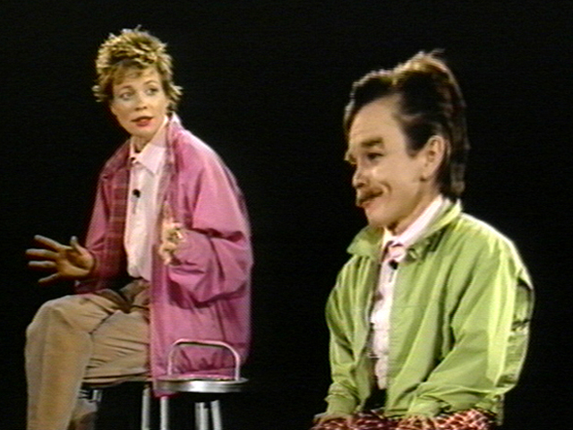 A woman on a stool looking at a person with a mustache